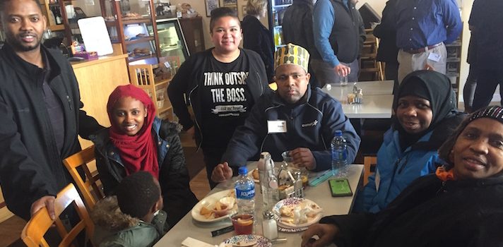 Five members of Isuken Co-op, a Somali-Bantu cooperative, join Mo Manklang of the US Federation of Worker Cooperatives at a table with snacks